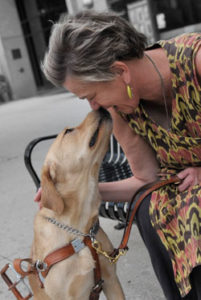 Author Beth Finke smiling and giving her Seeing Eye dog a smooch