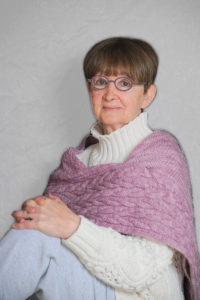 Picture of author Deanie Yasner wearing her signature round glasses with a lavender knitted wrap over a white turtleneck sweater